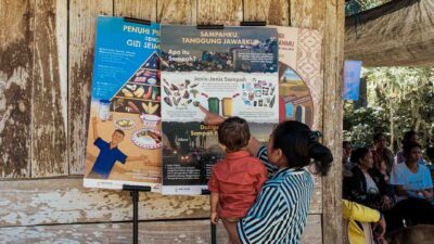 Mother holding her child beside waste, nutrition and malaria education posters in a remote East Sumba village.