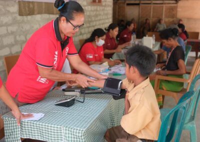 A health worker checks a boy’s blood pressure at a table, with other consultations taking place behind them.