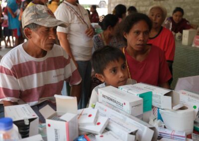 Adults and a child gather beside a table holding medicine boxes during the Bidi Hunga care day.