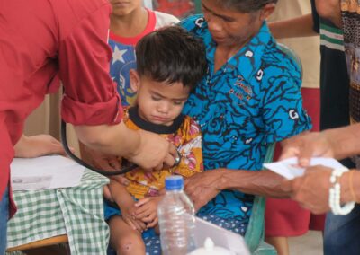 A clinician examines a young child with a stethoscope while the child sits on an adult’s lap.