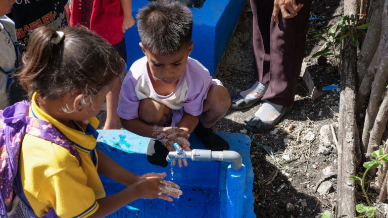 Kinder waschen Hände in einem blauen Waschbecken Zwei Kinder wischen ihre Hände mit Seifenwasser neben einem Wasserhahn über einem blauen Außenwaschbecken.