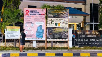 A person faces HIV and waste management health prevention billboards outside Puskesmas Waingapu.
