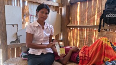Rambu Esther holds medicine beside a woman receiving community healthcare at home in East Sumba.