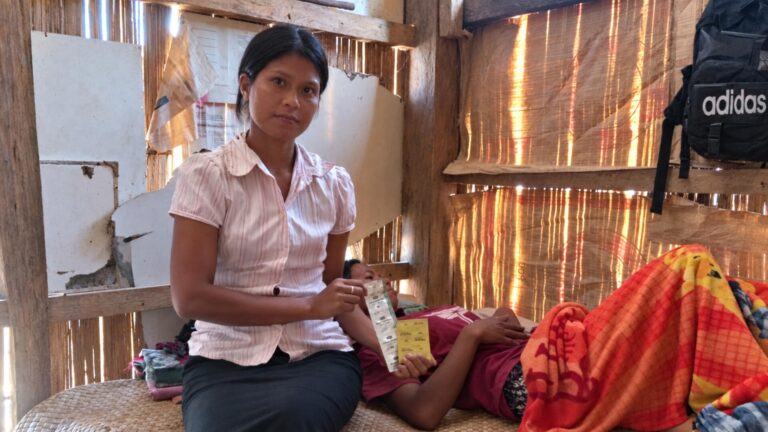 Rambu Esther holds medicine beside a woman receiving community healthcare at home in East Sumba.