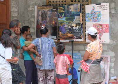 Adults and children gather in front of posters about smoking, alcohol, healthy food and handwashing in Bidi Hunga.