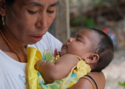 A woman in a white shirt cradles an infant dressed in yellow during the Bidi Hunga community care day.