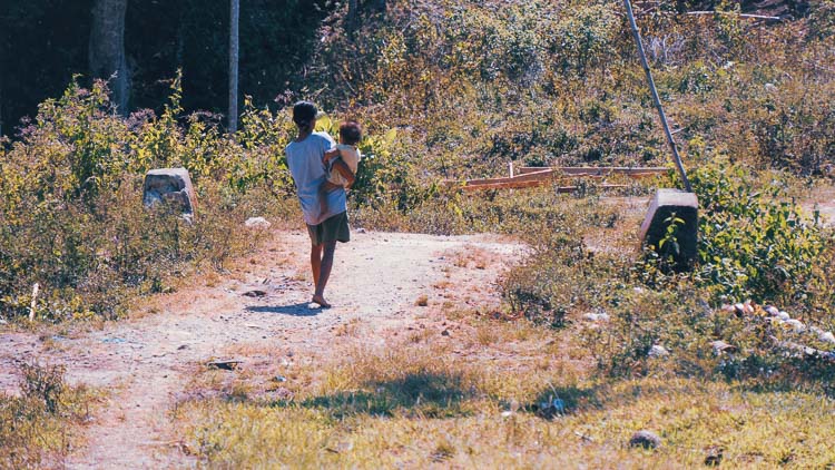 Un adulte portant un jeune enfant sur un chemin rural à Sumba
