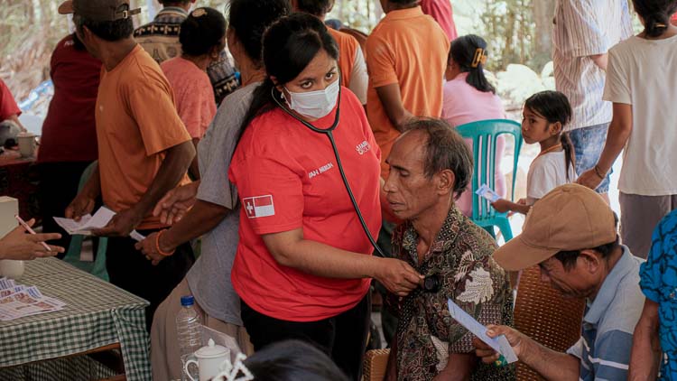 Female healthcare worker using a stethoscope to examine a male patient during a community medical care day in Bidi Hunga, East Sumba.