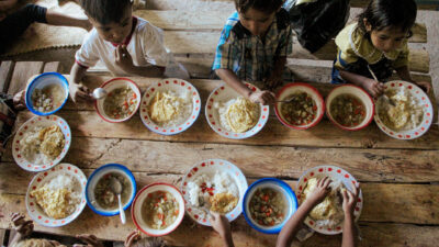 Children eat rice and soup around a wooden table during a shared meal in an East Sumba village.