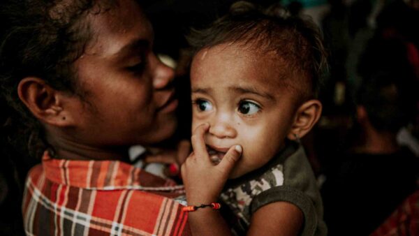 Young child held by a caregiver in rural Indonesia, illustrating vulnerability to preventable rubella and congenital health risks