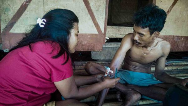 Village health agent treating patient at home in East Sumba illustrating geographic healthcare inequality