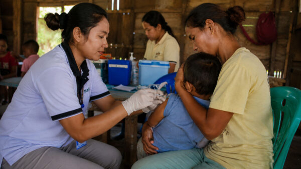 Kawan Sehat health agent vaccinates a child held by his mother during rural medical outreach in East Sumba.