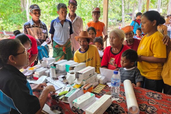 A health worker speaks with children and adults gathered around a table of medicines in Bidi Hunga.