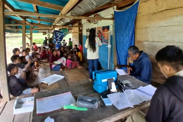 Desiana mène une campagne d’éducation sanitaire avec des affiches sur les tissus, tandis que des enfants et des adultes s’assoient à proximité Lahiru.